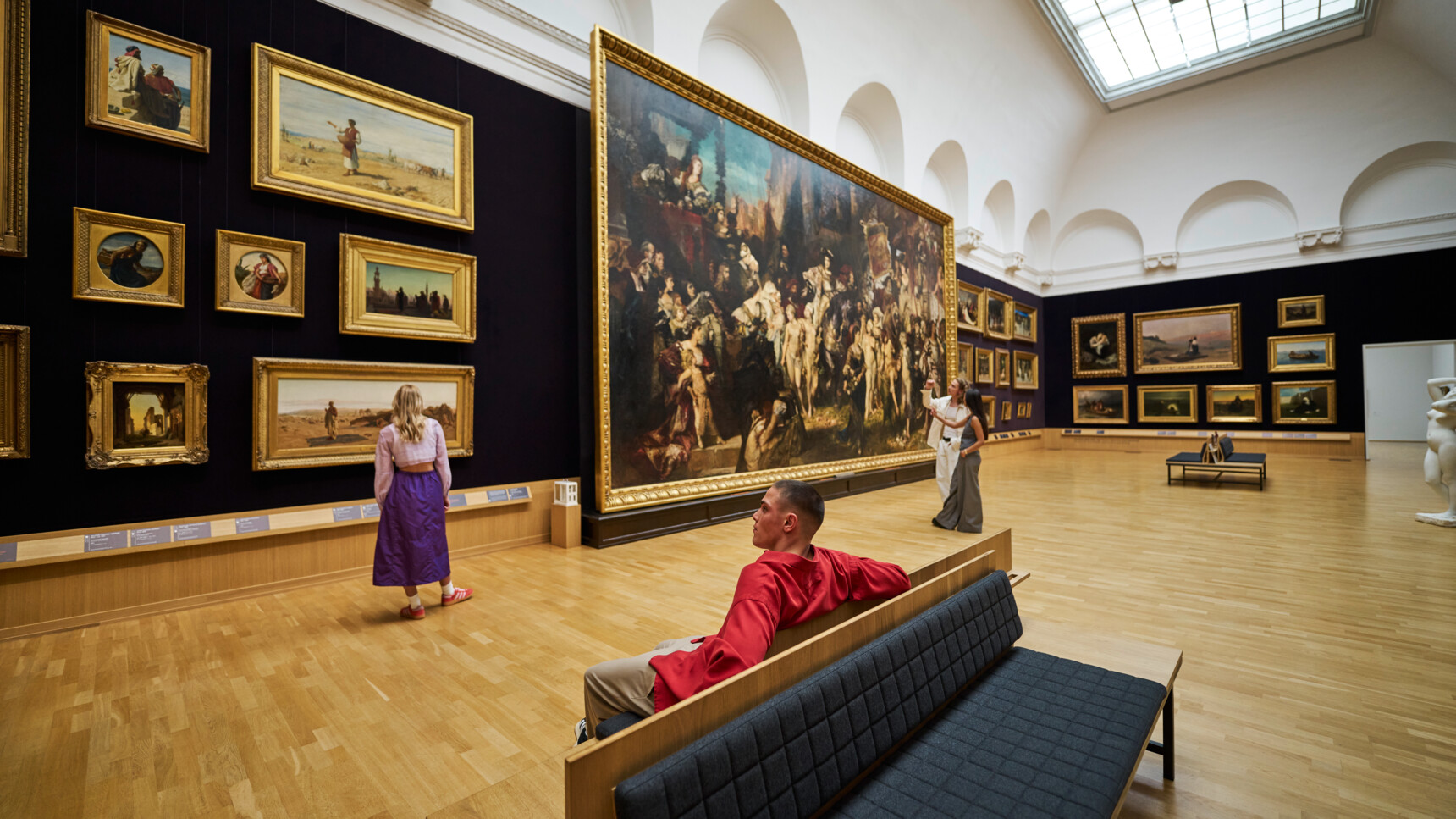Besucher betrachten Gemälde in einem großen, hellen Kunstmuseum mit Holzfußboden und hohen Decken.