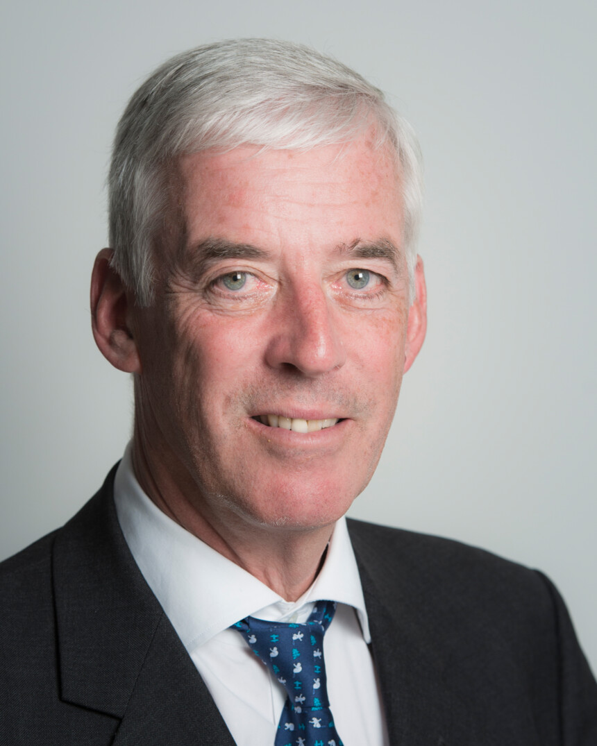 Porträt eines älteren Mannes mit grauen Haaren, Anzug und Krawatte in einem Büro.