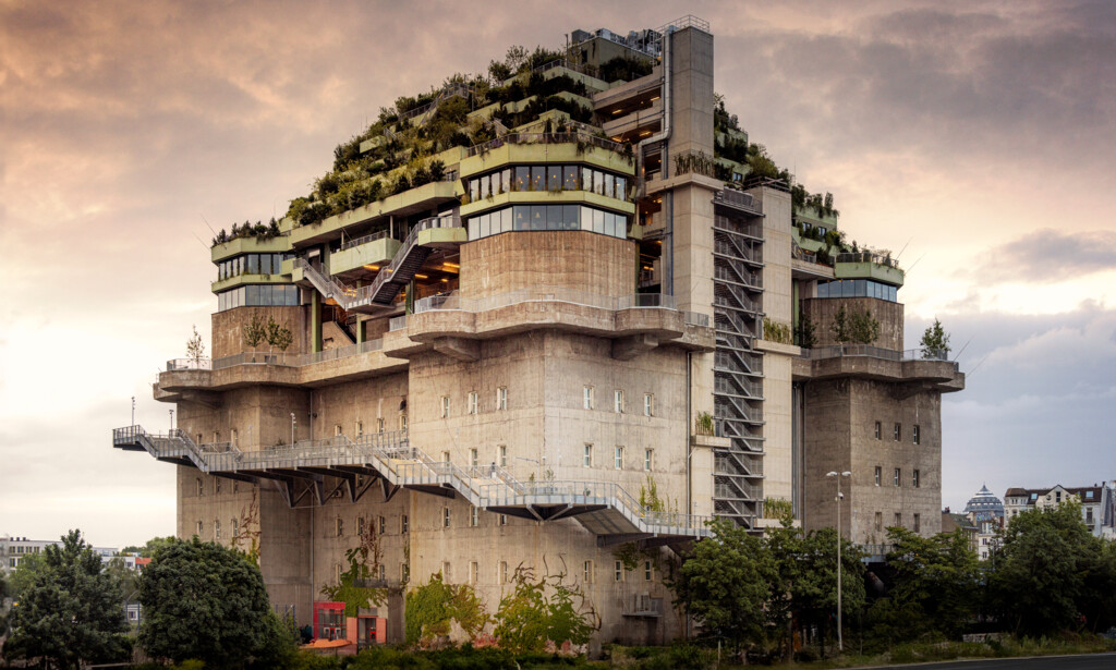 Brutalistisches Gebäude mit üppiger Dachbegrünung und mehreren Terrassen unter bewölktem Himmel.