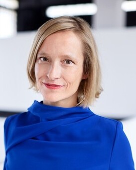 Portrait of a smiling woman with short blonde hair wearing a blue top in a bright indoor setting.