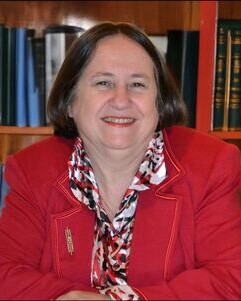 Porträt einer älteren Frau mit schulterlangen grauen Haaren und gemustertem Oberteil.