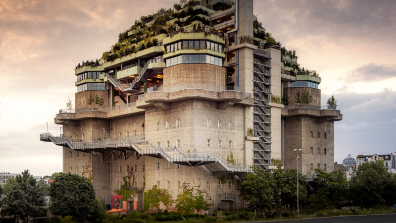 Brutalistisches Gebäude mit üppiger Dachbegrünung und mehreren Terrassen unter bewölktem Himmel.