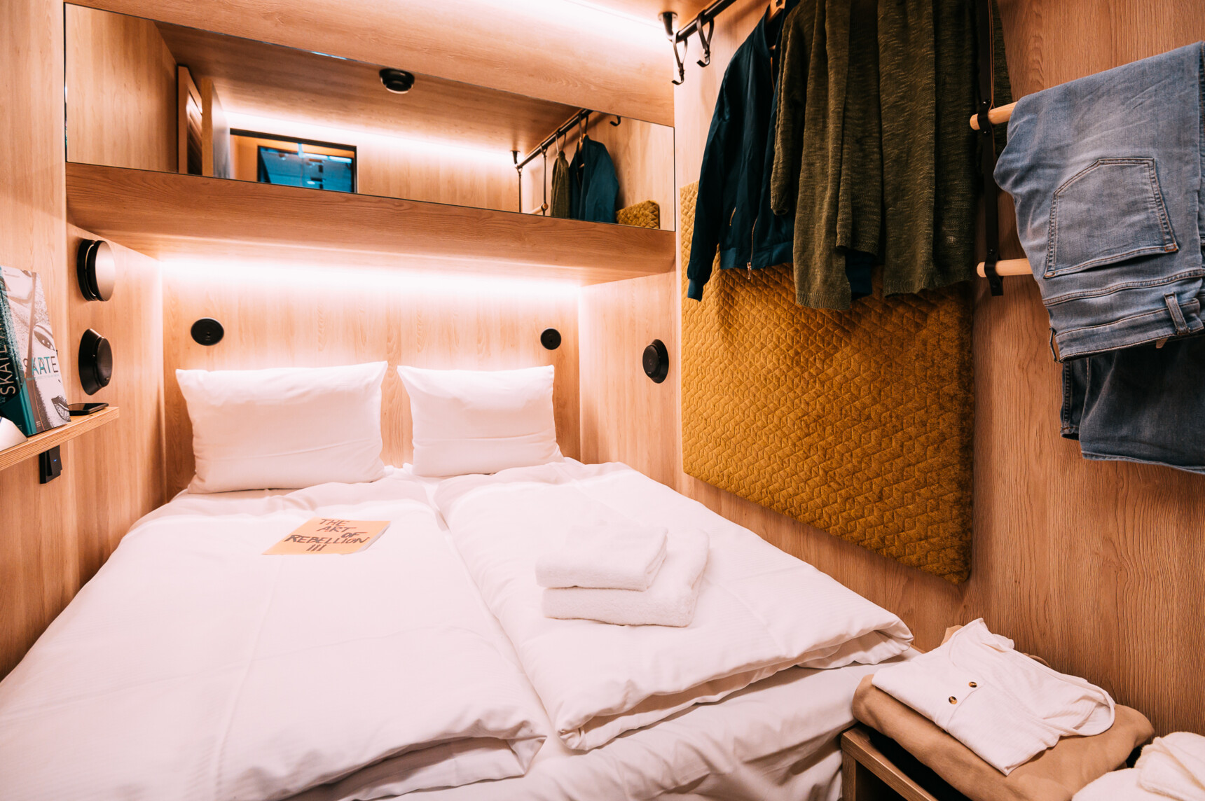 Kleines, gemütliches Schlafzimmer mit Holzverkleidung, Doppelbett, Spiegel und aufgehängter Kleidung.