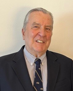 Portrait of an elderly man in a suit and striped tie smiling against a plain background.