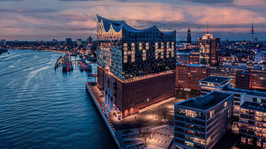 Die beleuchtete Elbphilharmonie am Hamburger Hafen bei Abenddämmerung mit Stadtpanorama.