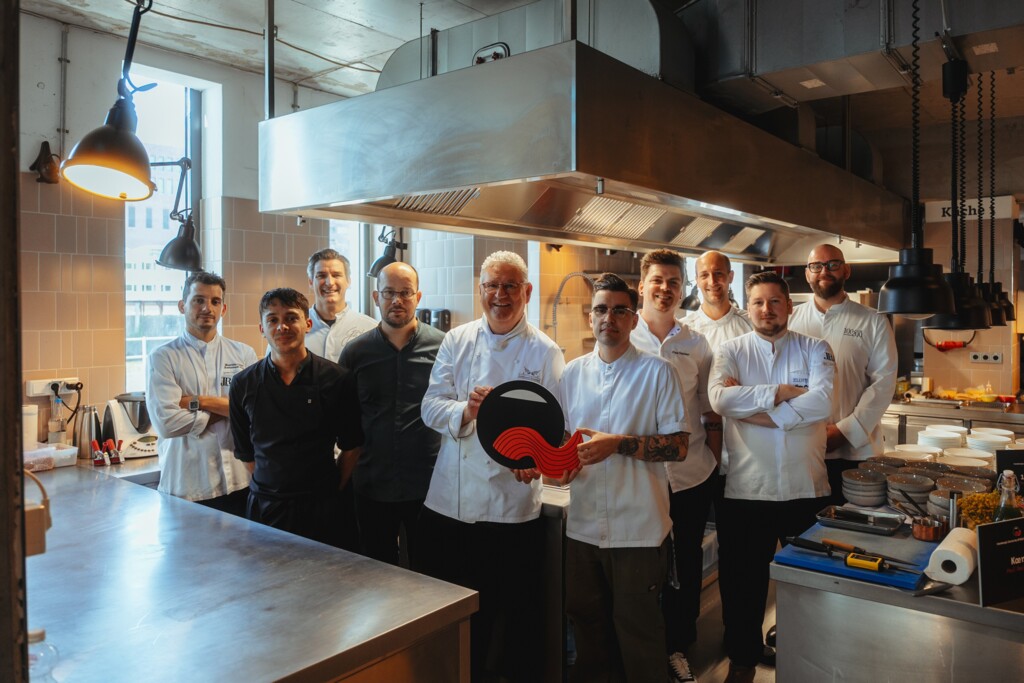 Küchenteam in Kochkleidung posiert gemeinsam in einer professionellen Restaurantküche.