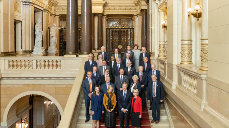 Gruppenfoto von 25 Personen in formeller Kleidung auf einer prächtigen Treppe in einem historischen Gebäude.