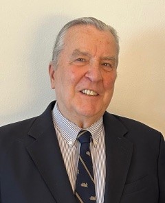 Portrait of an elderly man wearing a suit, striped shirt, and patterned tie against a plain background.