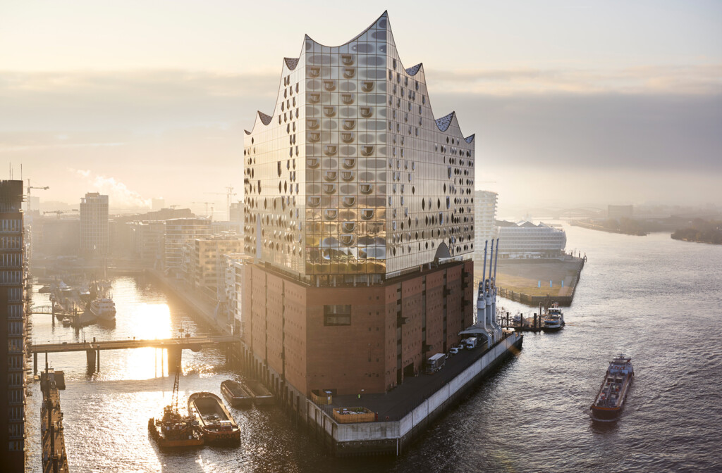Die Elbphilharmonie in Hamburg bei Sonnenaufgang mit Hafen und vorbeifahrenden Schiffen.