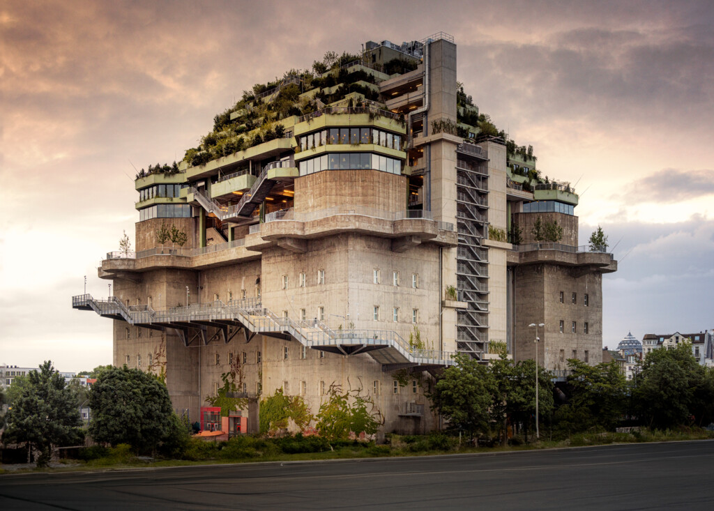 Brutalistisches Gebäude mit üppiger Dachbegrünung und mehreren Terrassen unter bewölktem Himmel.