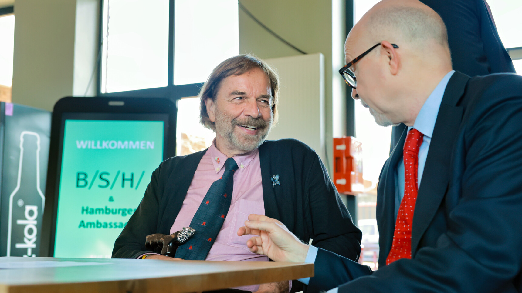 Two men in suits having a friendly conversation at a table in a bright room.