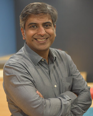 Portrait of a smiling man with folded arms wearing a grey shirt against a blurred background.