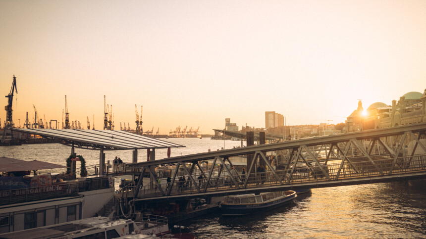 Sonnenuntergang über dem Hamburger Hafen mit Kränen, Brücke und Booten im Wasser.