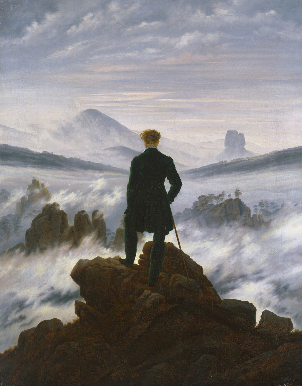 Ein Mann steht auf einem Felsen und blickt auf nebelverhangene Berge und Täler.