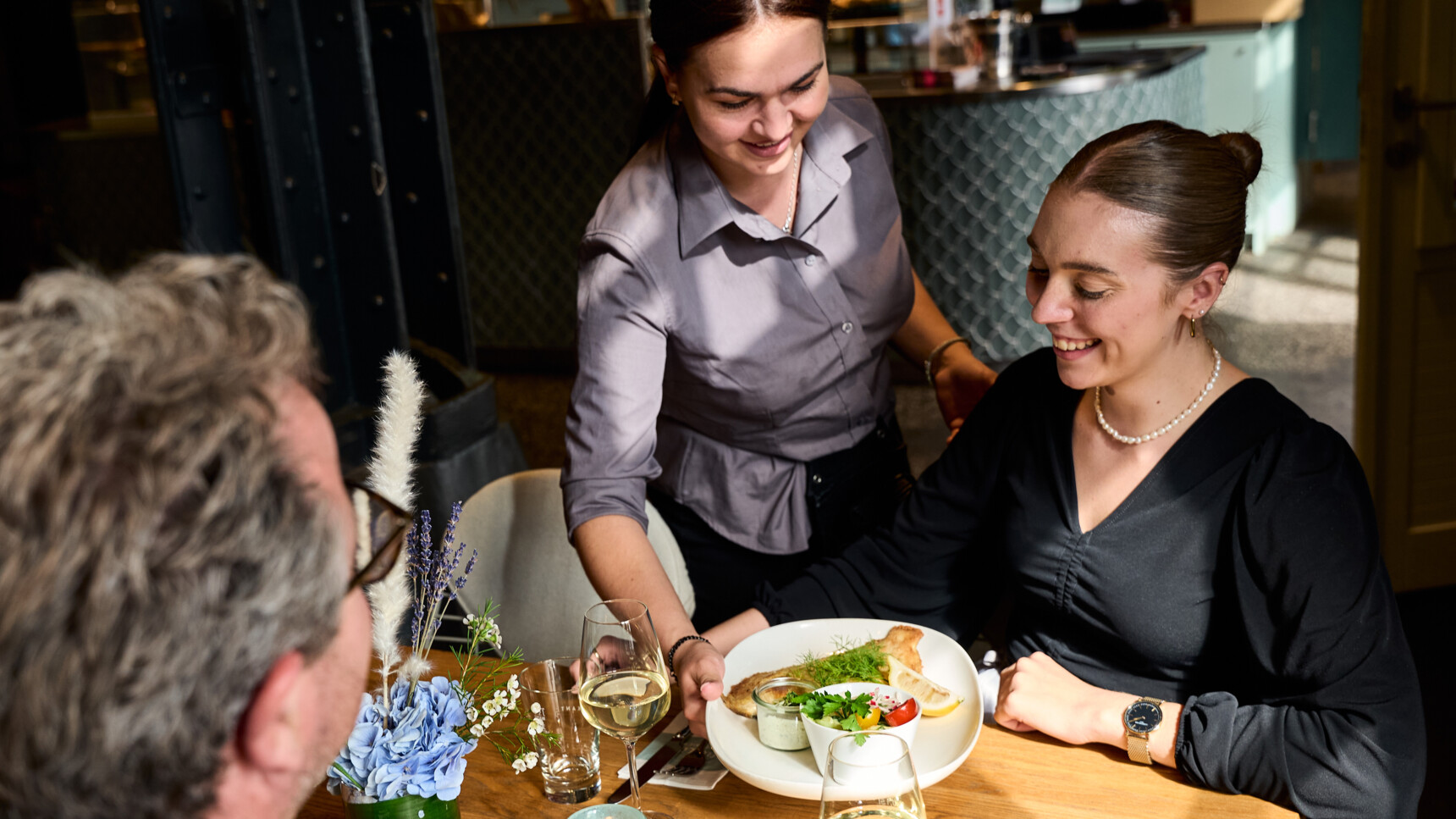 Eine Kellnerin serviert einem Paar in einem Restaurant ein Gericht mit Salat und Fisch.