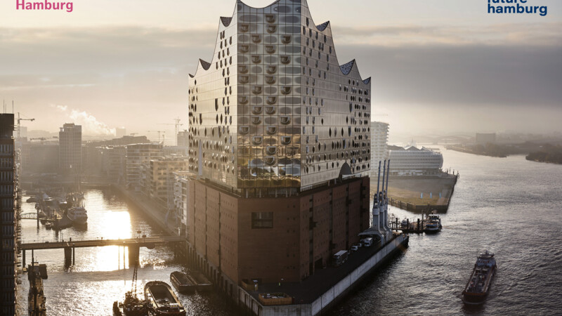 Die Elbphilharmonie im Hamburger Hafen bei Sonnenaufgang mit vorbeifahrenden Schiffen.