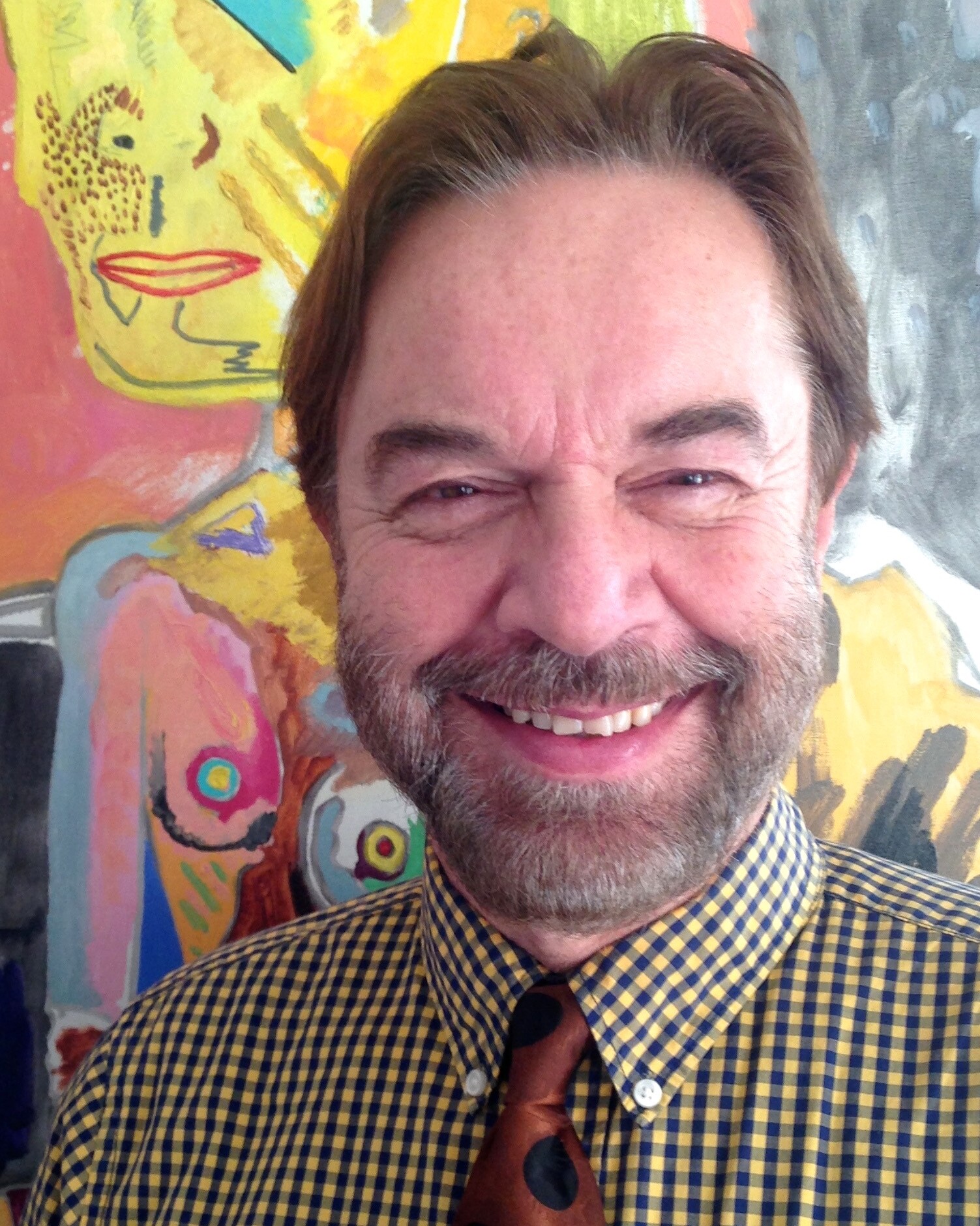 Porträt eines lächelnden Mannes mit Bart vor einem farbenfrohen abstrakten Gemälde.