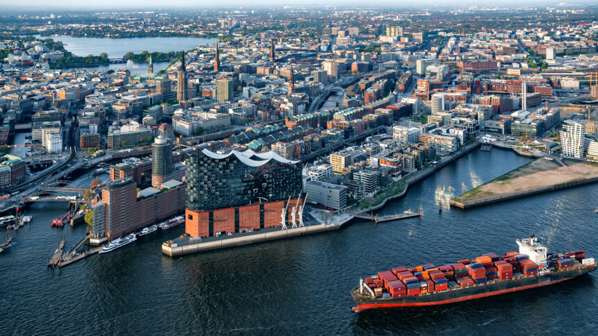 Luftaufnahme des Hamburger Hafens mit Elbphilharmonie und einem Containerschiff auf der Elbe.