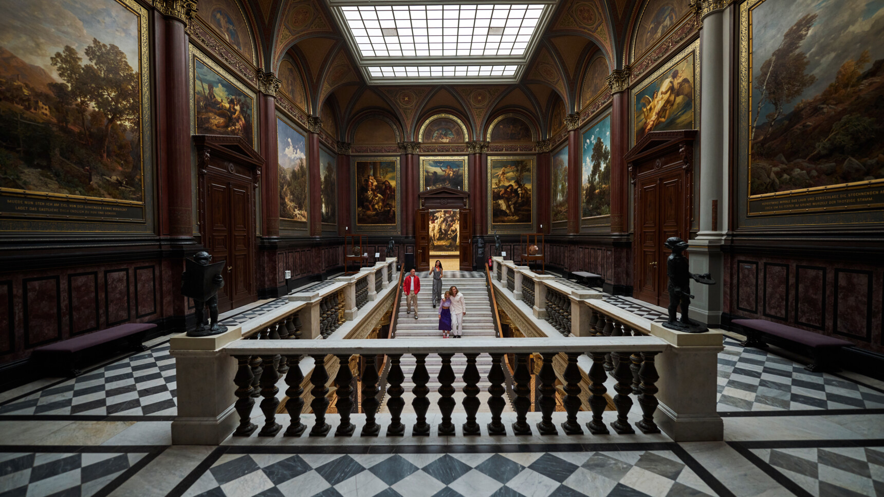 Magnificent museum hall with large paintings, marble floor and staircase for visitors to walk up.
