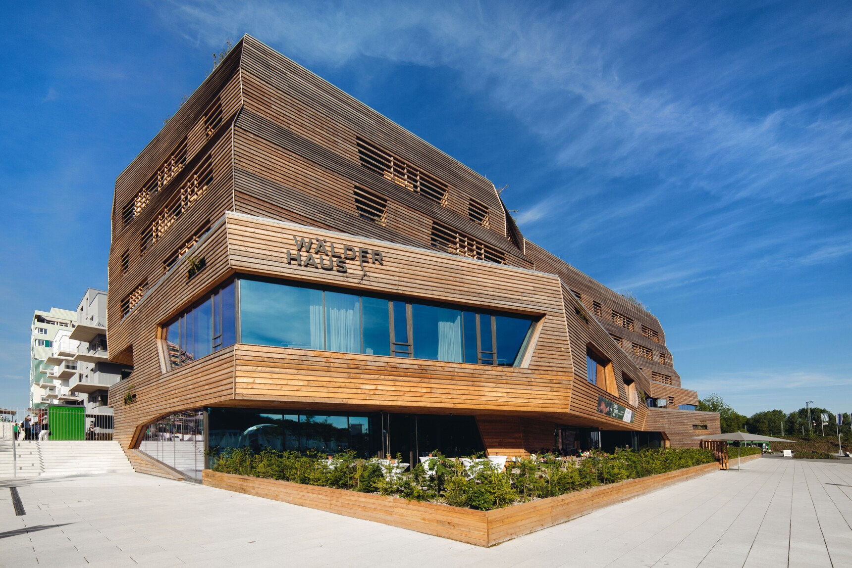 Modernes, mehrstöckiges Holzgebäude mit großen Fenstern und der Aufschrift "Wälder Haus" bei sonnigem Wetter.