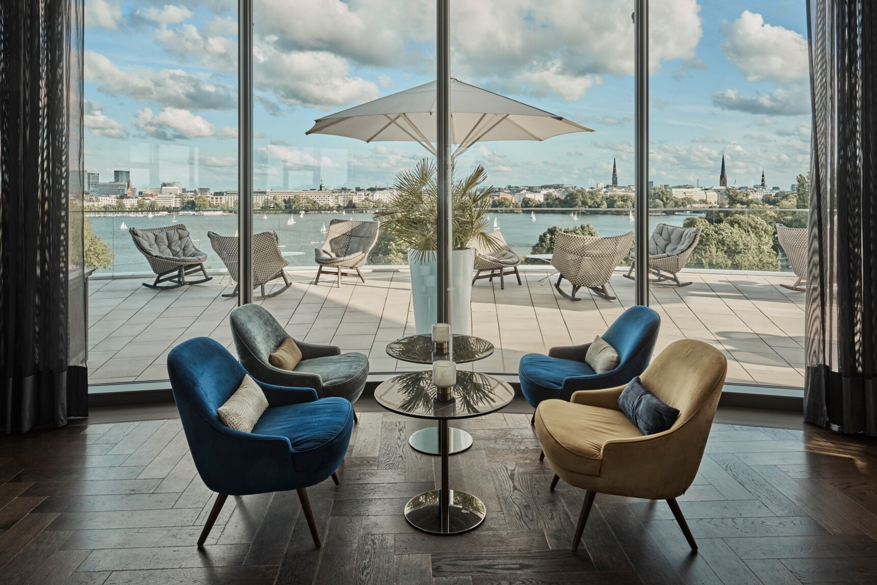 Gemütliche Sitzgruppe vor bodentiefen Fenstern mit Blick auf Terrasse, See und Stadtpanorama bei Tageslicht.