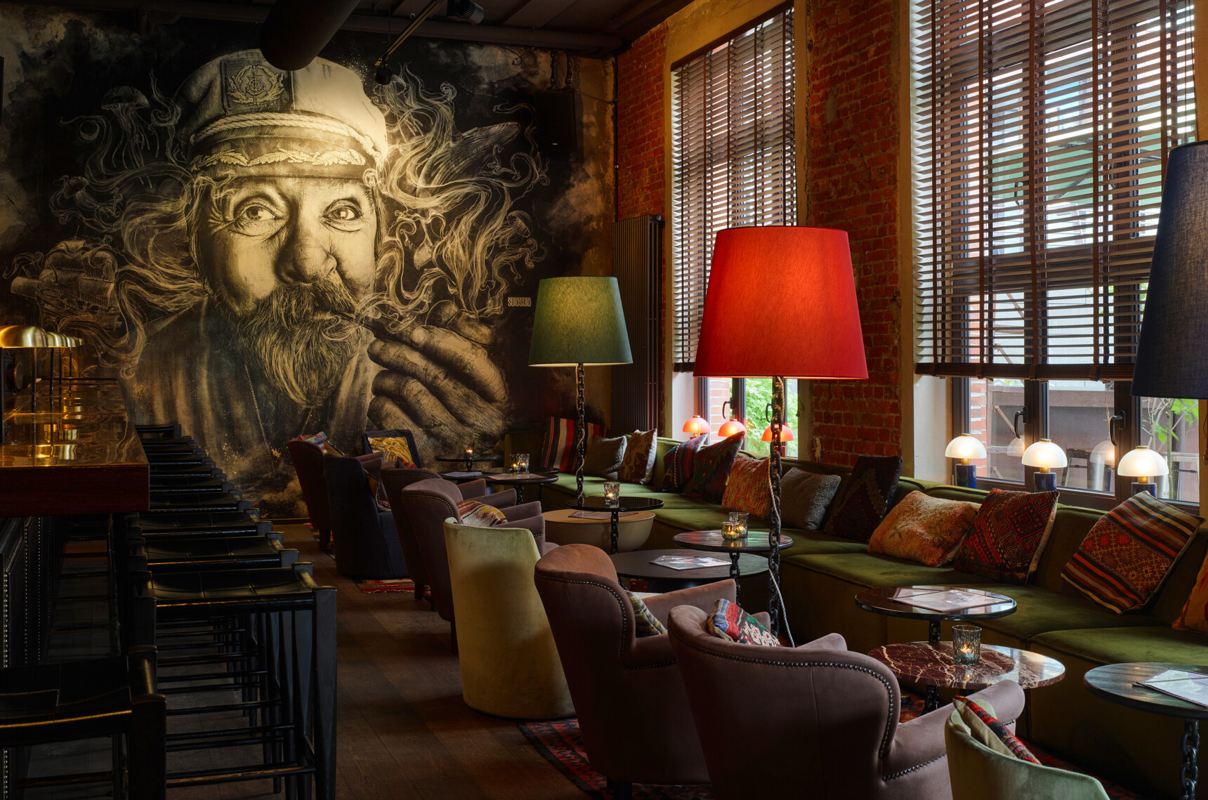 Gemütliche Bar mit bunten Lampen, Sitzgelegenheiten und großer Wandmalerei eines rauchenden Seemanns.