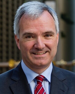 Porträt eines lächelnden Mannes mit grauen Haaren, Anzug und rot-weiß gestreifter Krawatte.