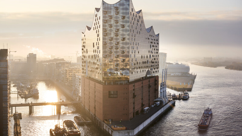 Die Elbphilharmonie Hamburg mit Glasfassade und Wellenform bei Sonnenaufgang am Wasser.
